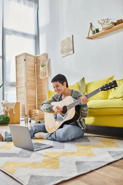 Tiro vertical de la mujer sentada en el suelo con la guitarra sonriendo a la cámara portátil, la educación en casa - foto de stock