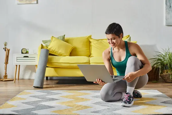 Gioiosa giovane donna in piedi su un ginocchio sul pavimento sorridente alla fotocamera del computer portatile, fitness e sport — Foto stock