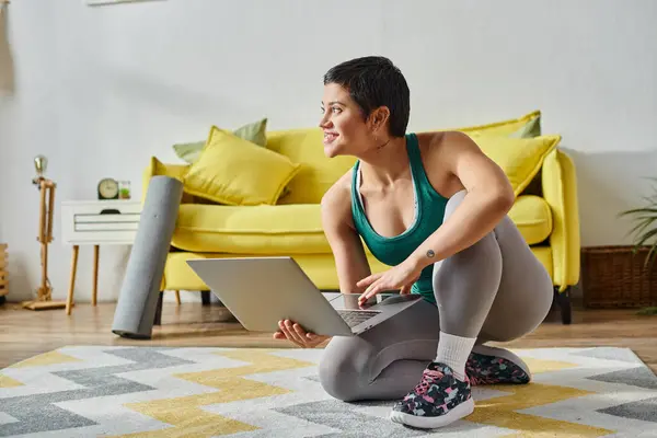 Mujer sonriente de buen aspecto en ropa deportiva posando con el ordenador portátil antes de la lección, fitness y deporte - foto de stock