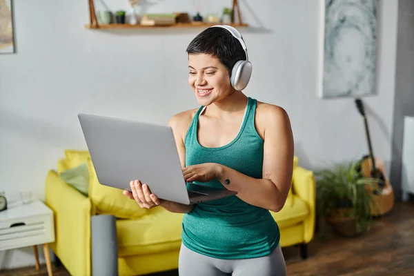 Happy young woman with laptop and headphones attending remote fitness lesson, fitness and sport — Stock Photo