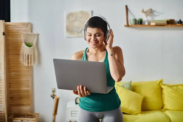 Cheerful short haired woman with headphones looking at laptop camera during online fitness lesson — Stock Photo
