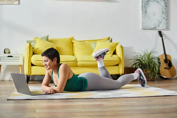 Cheerful woman lying on floor and smiling at laptop camera at remote sport lesson, fitness and sport — Stock Photo