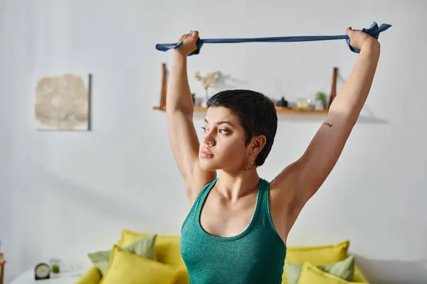 Attractive short haired woman with tattoo exercising with resistance band and looking away — Stock Photo