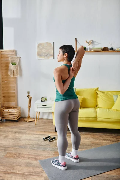 Tiro vertical de mujer atlética joven con el pelo corto que estira sus brazos activamente, aptitud — Stock Photo
