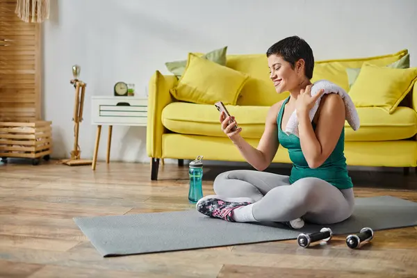 Mujer atractiva alegre en ropa deportiva sonriendo en su teléfono móvil relajándose después de hacer ejercicio — Stock Photo