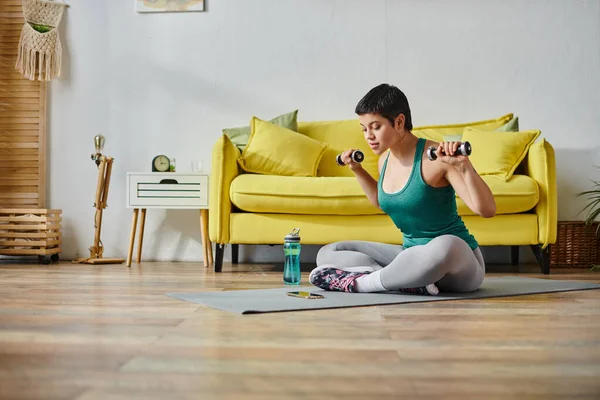 Atractiva mujer deportiva con el pelo corto haciendo ejercicio con pesas y mirando a su teléfono móvil — Stock Photo