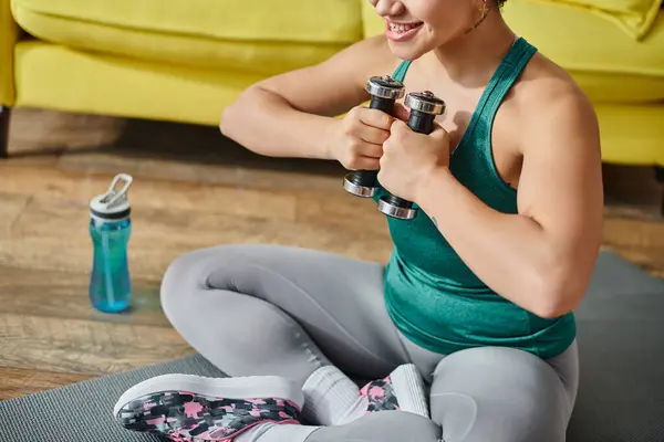 Ausgeschnittene Ansicht einer jungen Smiley-Frau, die auf dem Boden sitzt und mit Hanteln, Fitness und Sport trainiert — Stockfoto
