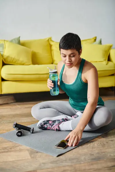Plan vertical de femme relaxante focalisée avec bouteille d'eau à la main en regardant son mobile, remise en forme — Photo de stock