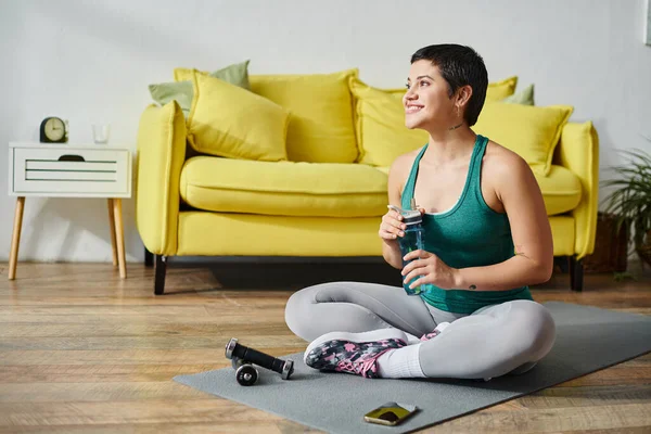 Alegre mujer guapa en ropa deportiva sosteniendo botella de agua y sonriendo felizmente, fitness y deporte — Stock Photo