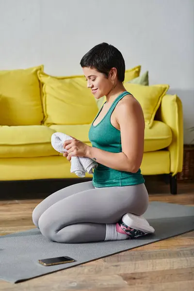 Plan vertical de femme gaie en vêtements de sport avec tatouage assis sur le sol avec serviette, fitness — Photo de stock