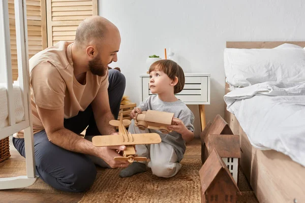 Joyful modern father and son in cozy homewear playing with wooden toys and looking at each other — Stock Photo