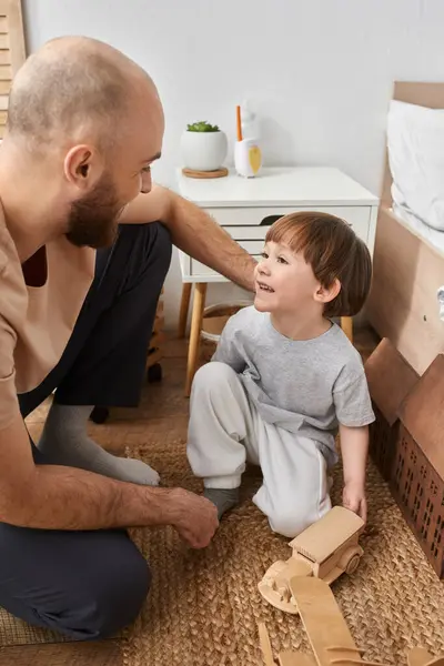 Joyeux petit garçon souriant à son père barbu pendant qu'ils jouent avec des jouets en bois, famille — Photo de stock