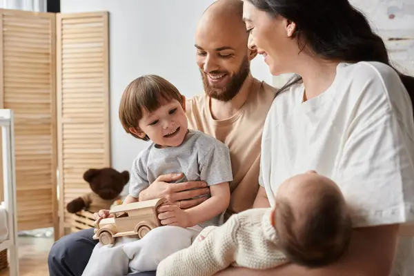 Happy little boy in homewear sitting with his parents on bed and looking at his newborn brother — Stock Photo