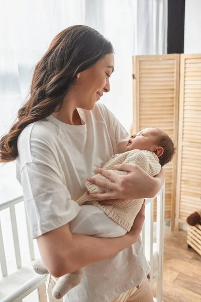 Vertikale Aufnahme einer jungen schönen Mutter, die ihr neugeborenes Baby hält und es liebevoll anlächelt, Familie — Stockfoto