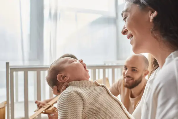 Focus on happy mother looking at her newborn baby with blurred joyful father on backdrop, family — Stock Photo