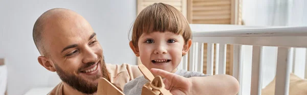 Lustiger netter Junge, der mit einem Holzflugzeug spielt, sein Vater lächelt in die Kamera, Familienkonzept, Banner — Stockfoto