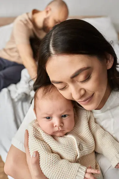 Focus on loving mother holding her newborn baby with blurred father on backdrop, family concept — Stock Photo