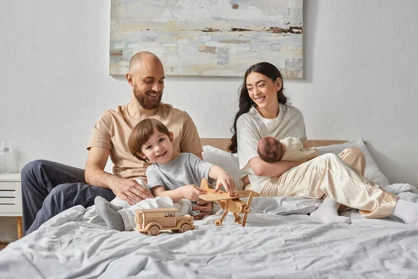 Familia alegre pasar un buen rato juntos relajarse en la cama y sonreír el uno al otro, crianza moderna - foto de stock
