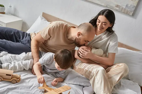 Happy mother holding newborn baby while her husband kissing his forehead next to little son, family — Stock Photo