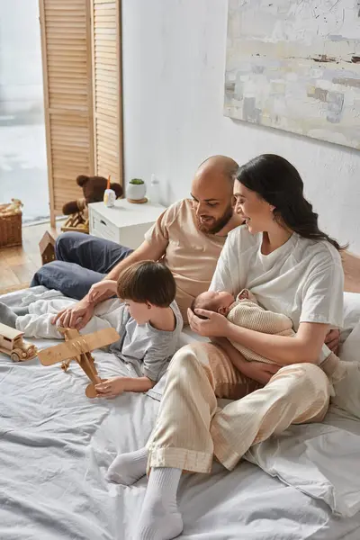 Vertikale Aufnahme einer jungen fröhlichen Familie, die es sich gut gehen lässt, zusammen im Bett zu liegen, moderne Elternschaft — Stockfoto