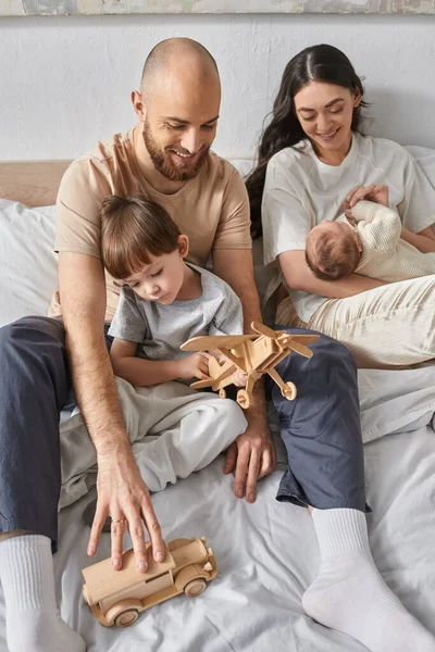 Tiro vertical de los padres modernos pasar tiempo de calidad con su hijo pequeño y el bebé recién nacido, la familia - foto de stock