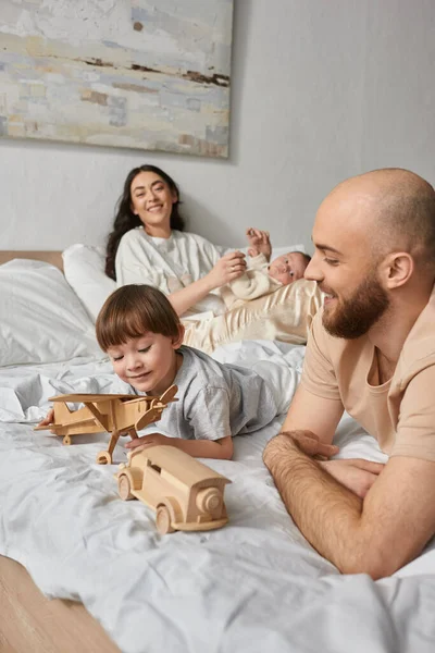 Vertical shot of father playing with his little son with blurred wife and newborn baby on backdrop — Stock Photo