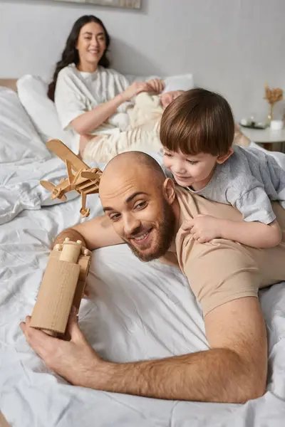 Focus on bearded father playing with wooden toys with his son next to blurred wife and newborn baby — Stock Photo