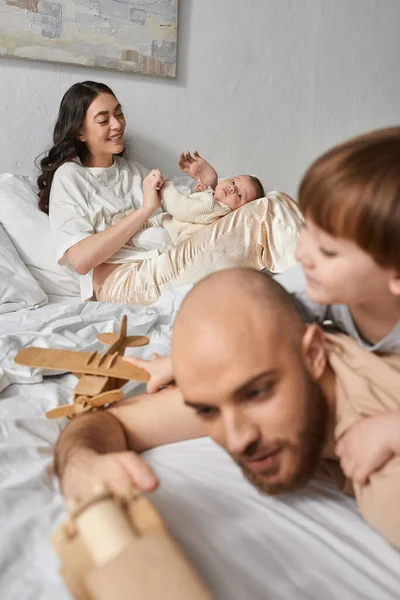 Focus on happy mother holding her newborn baby boy next to her blurred husband and little son — Stock Photo