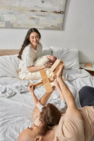 Cheerful mother holding newborn baby looking happily at her husband playing with their little son — Stock Photo