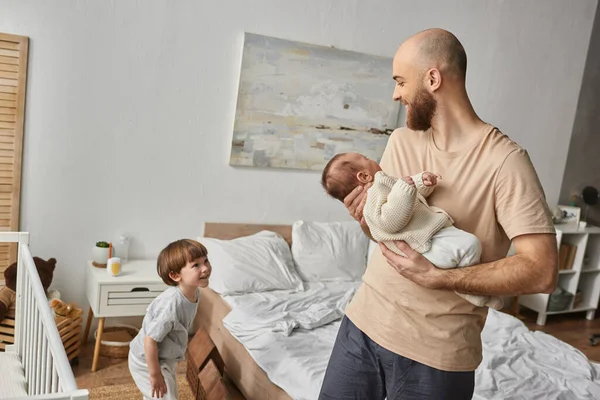 Joyeux père barbu tenant son nouveau-né et souriant joyeusement à son petit fils, sa famille — Photo de stock