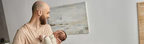 Alegre padre barbudo sosteniendo a su bebé recién nacido y sonriendo felizmente, concepto de familia, bandera - foto de stock