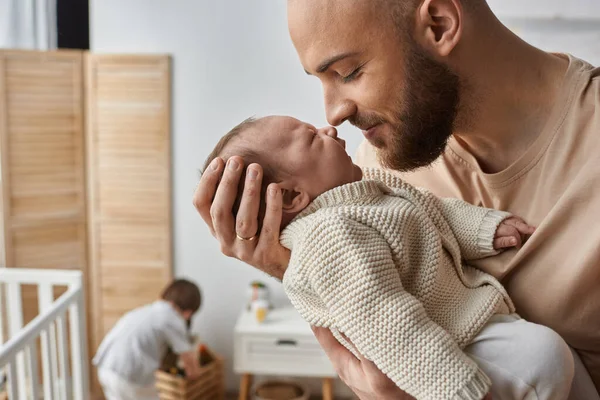 Focus on father holding lovingly his newborn baby with his little son playing on backdrop, family — Stock Photo