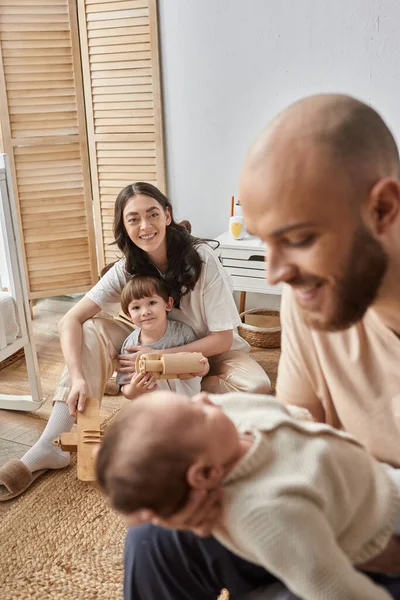 Tiro vertical de la madre feliz con su pequeño hijo mirando borrosa marido y bebé recién nacido - foto de stock