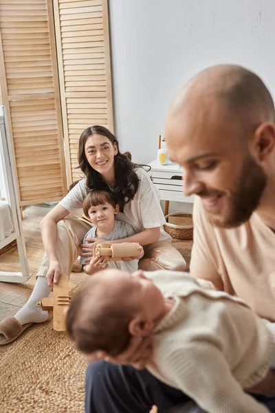 Vertical shot of happy mother with her little son looking at blurred husband and newborn baby — Stock Photo