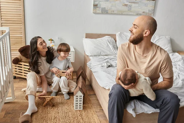 Cheerful modern parents spending time with their children in their bedroom smiling at each other — Stock Photo