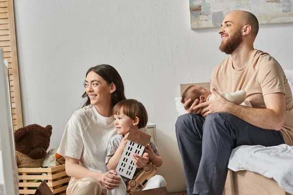 Alegre familia feliz en ropa cómoda sonriendo alegremente y mirando hacia otro lado, crianza moderna - foto de stock