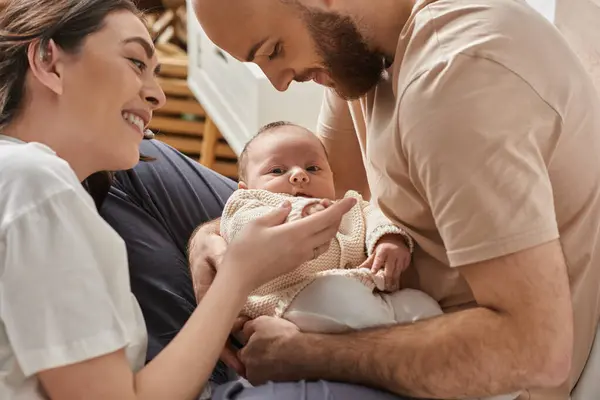 Padres modernos alegres sosteniendo a su bebé recién nacido lindo y sonriéndole, concepto de familia - foto de stock