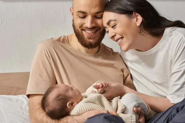 Joyeux parents aimants en vêtements de maison souriant chaleureusement à leur nouveau-né garçon, concept de famille — Photo de stock
