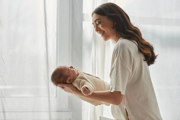 Young cheerful mother smiling happily and holding her cute newborn baby boy, family concept — Stock Photo