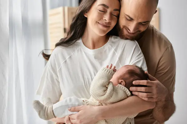 Joyous modern parents in cozy homewear hugging warmly and holding their newborn son lovingly, family — Stock Photo