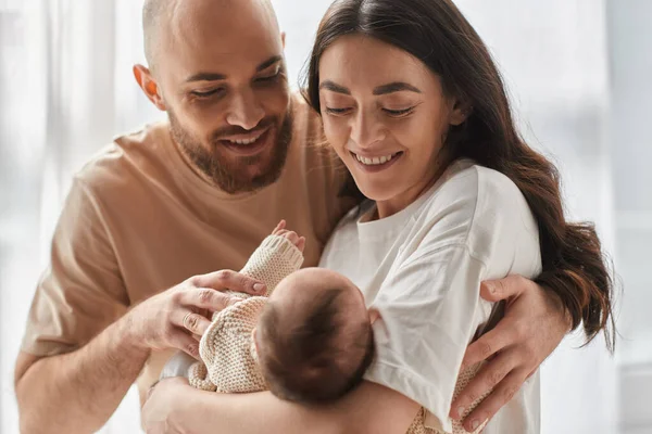 Joyous happy parents in cozy homewear smiling happily at their newborn baby boy, family concept — Stock Photo