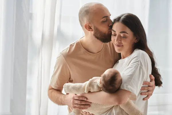 Beautiful mother holding her newborn baby while her husband kissing her in forehead, family — Stock Photo