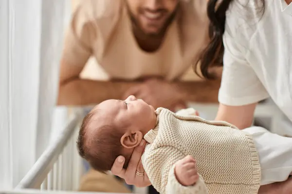 Focus on adorable newborn baby lying in his mother arms next to his blurred bearded jolly father — Stock Photo