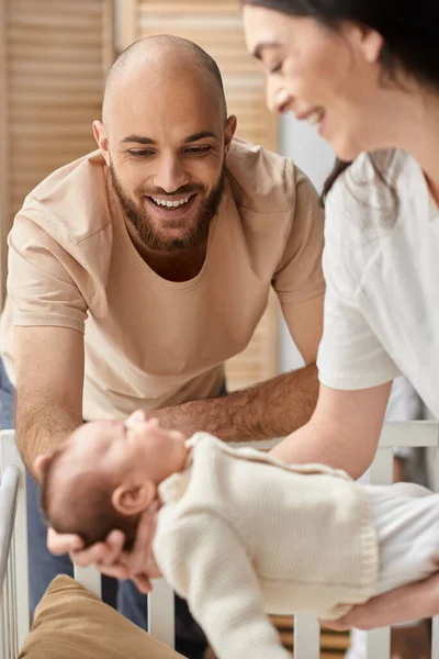 Vertical focused shot of bearded happy father looking at his blurred wife holding their newborn baby — Stock Photo