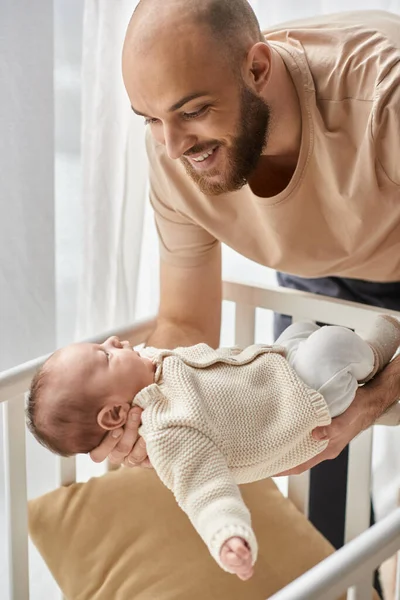 Vertikale Aufnahme eines bärtigen glücklichen Vaters, der seinen neugeborenen Sohn in die Krippe legt, Familienkonzept — Stockfoto