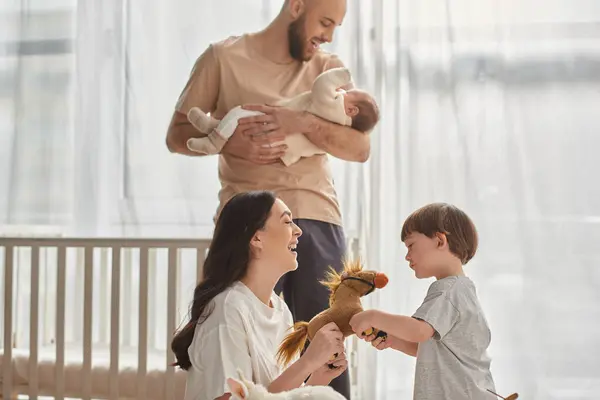 Concentre-se em mãe brincando com cavalo de brinquedo com seu filho pequeno ao lado de seu marido borrado e bebê menino — Fotografia de Stock