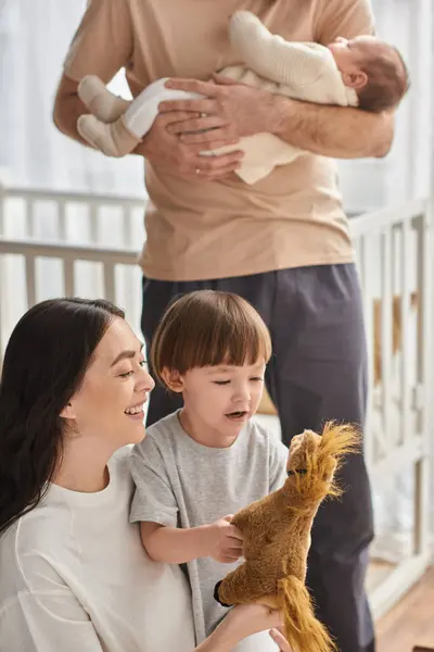 Tiro vertical de mãe alegre brincando com seu filho com cavalo de brinquedo, conceito de família — Fotografia de Stock