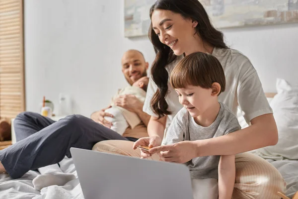 Fokus auf freudige Mutter mit kleinem Sohn, die auf Laptop mit Kreditkarte blickt, Familienkonzept — Stockfoto