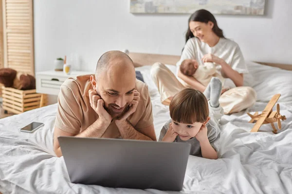 Se concentrer sur le père heureux et le petit fils regarder un film sur ordinateur portable à côté de sa femme floue et bébé garçon — Photo de stock