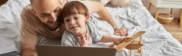 Adorable little boy with wooden plane in hand looking at laptop with his bearded father, banner — Stock Photo